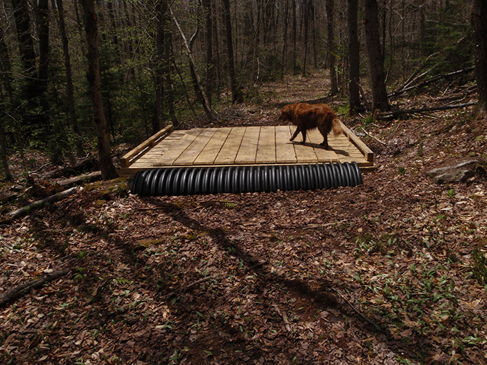 The Seventh Lake Mountain Trail, a class II community connector snowmobile trail, includes use of non-natural materials like the half culvert pictured above to create ramps for snowmobiles and groomers to access a bridge. This is a design feature that is not used for foot trails.